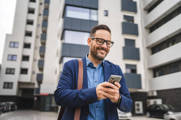 Adult businessman stand in front modern business center and use mobile phone