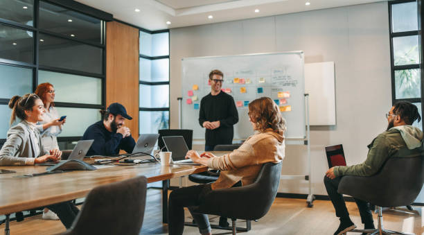 Professionals in a diverse group collaborate in a boardroom, engaging in a lively brainstorming session. They discuss ideas, showcasing teamwork and creativity. This successful tech company employs effective project management and the Scrum process. A dynamic workplace embracing innovation and productive conversation.