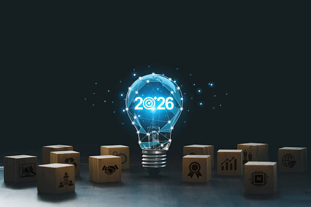 Futuristic light bulb with 2026 and a bullseye glows above wooden blocks of strategy icons, symbolizing innovation, business goals, AI, growth, quality and sustainability for planning and success.